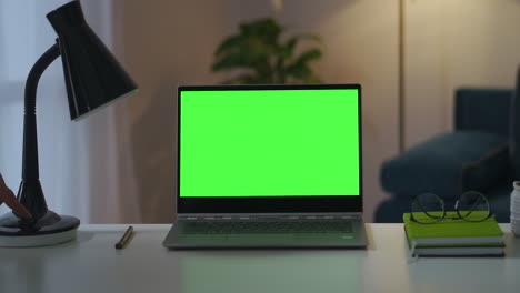 man-is-turning-off-table-and-floor-lamps-in-working-room-notebook-with-green-screen-for-chroma-key-technology-interior-of-home-office
